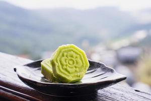 heerlijke groene mungbooncake met zwarte theeplaat op houten balustrade van een theehuis in taiwan met prachtig landschap op de achtergrond, close-up. foto