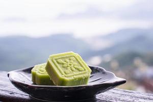 heerlijke groene mungbooncake met zwarte theeplaat op houten balustrade van een theehuis in taiwan met prachtig landschap op de achtergrond, close-up. foto