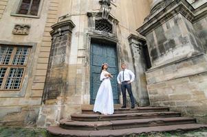 bruiloft fotosessie op de achtergrond van het oude gebouw. de bruidegom kijkt naar zijn bruid die poseert. rustieke of boho huwelijksfotografie. foto