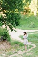 portret van een jong mooi meisje in een zomerjurk. zomer fotosessie in het park bij zonsondergang. een meisje zit onder een boom in de schaduw. foto