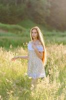 portret van een jong mooi meisje in een zomerjurk. zomer fotosessie in het park bij zonsondergang. een meisje zit onder een boom in de schaduw. foto