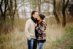 gelukkige paar verliefd in de herfst. gekrulde besnorde man en roodharige vrouw in leren jassen en jeans omhelzen elkaar teder. meisje maakt handpalmen foto