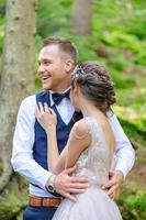 een aantrekkelijk pasgetrouwd stel, een gelukkig en vreugdevol moment. een man en een vrouw scheren en kussen in vakantiekleren. bohemien-stijl bruiloft cermonia in het bos in de frisse lucht. foto