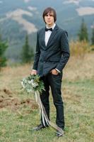 knappe elegante bebaarde bruidegom in geruit pak staat op de brug in het bos. stijlvolle bruiloft bruidegoms foto in bruine leren schoenen. rustieke hipster portret.