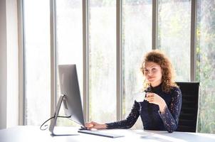aantrekkelijke mooie en zelfverzekerde zakenvrouw die met de computer werkt en koffie drinkt in het moderne kantoor of thuis foto