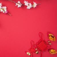 ontwerpconcept van chinees nieuw maanjaar - mooie chinese knoop met pruimenbloesem geïsoleerd op rode achtergrond, plat lag, bovenaanzicht, overhead lay-out. foto