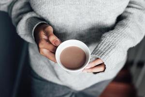 vrouwenhanden die winterkleren met lange mouwen dragen en een kop warme chocolademelk vasthouden foto