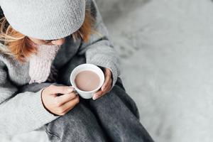 een meisje met winterkleren die in de winter thuis genieten van een kopje warme drank foto