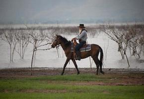 silhouetcowboy te paard tegen een prachtige zonsondergang, cowboy en paard bij het eerste licht, berg, rivier en levensstijl met natuurlijke lichte achtergrond foto