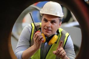 mannen industrieel ingenieur die een veiligheidshelm draagt terwijl hij in een zware industriële fabriek staat. het onderhoud van het werken aan industriële machines en het controleren van de installatie van het beveiligingssysteem in de fabriek. foto