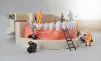 miniatuurmensen om een tand of een kleine figuur te repareren die tandmodel schoonmaakt als medisch en gezondheidszorg. foto