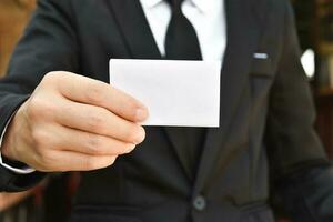 close-up van zakenman met wit stuk papier in zwart pak. idee voor zakelijke creditcard of visitekaartje. foto