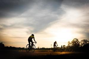 het paar wielrenners die op de racefiets rijden bij zonsondergang, silhouetbeeld. foto