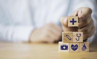 arts die het pictogram voor gezondheidszorg zet dat het scherm afdrukt op het stapelen van houten kubus voor het concept van de medische zorgverzekering. foto