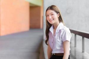 portret van een volwassen thaise student in universitair uniform. Aziatisch mooi meisje zit, ontspannen, glimlachend en gelukkig. foto