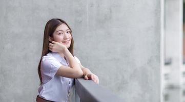 portret van een volwassen thais studentenmeisje in universitair studentenuniform. Aziatische mooi meisje zit gelukkig lachend op de universiteit. foto