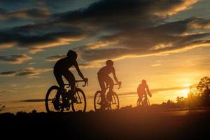 de mannen fietsen bij zonsondergang met een oranjeblauwe hemelachtergrond. abstracte silhouet achtergrond concept. foto