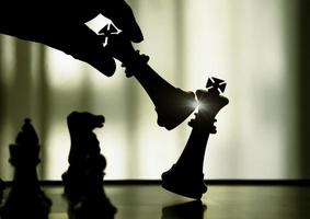 hand met zwarte koning aanval witte koning van schaken silhouetten strijd aan boord. zwarte koning zijn leider om met teamwork naar de overwinning te vechten. leider, strategie en schaakmat concept voor succes. foto