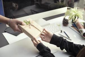 zakelijke vrouwen handen met kleine geschenkdoos op kantoor tafel, ze kijkt naar geschenkdoos verpakt ambachtelijk papier met lint en gevoel van geluk. kerst, nieuwjaar of valentijnsdag concept foto