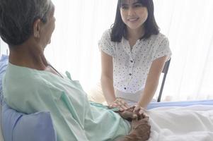 jonge dochter op bezoek bij zieke oude vader in ziekenhuis, gezondheidszorg en medisch concept foto