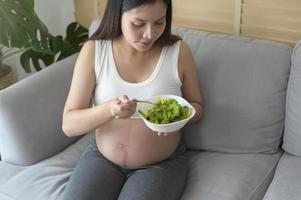 jonge zwangere vrouw met salade thuis, gezondheidszorg en zwangerschapszorg foto