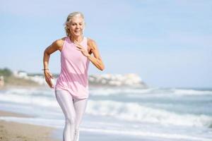 oudere vrouw die aan sport doet om fit te blijven. volwassen vrouw loopt langs de oever van het strand. foto