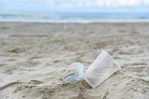 afval in de zee met plastic fles, plastic beker en schuimdoos op strand zanderige vuile zee foto