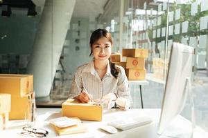 startende kleine bedrijven mkb-eigenaren vrouwelijke ondernemers schrijven het adres op de kassabon en controleren online bestellingen om zich voor te bereiden op het inpakken van de dozen, verkopen aan klanten, mkb-bedrijfsideeën online. foto