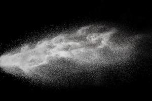 bevriezen beweging van witte stofdeeltjes op zwarte achtergrond. explosie van wit poeder. foto