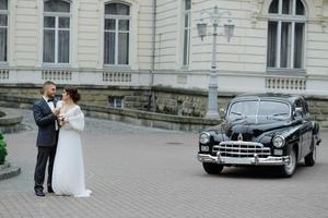 gelukkig luxe bruidspaar zoenen en omarmen in de buurt van retro met boeketauto in de herfst foto