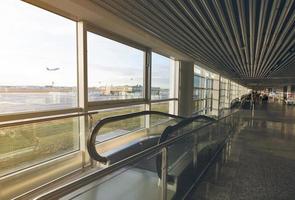 roltrap in de internationale luchthaventerminal op wazige passagiers die op de luchthaven lopen. luchthavengebouw met glazen raam. roltrap voor snelle passagiersbewegingen op de luchthaven. reisconcept. foto