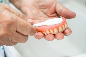 Aziatische senior of oudere oude vrouw patiënt gebruikt tandenborstel om gedeeltelijke prothese van vervangende tanden schoon te maken. foto