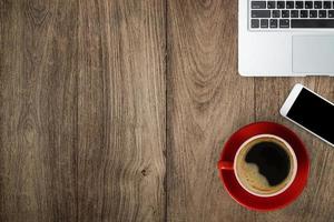 villen rood bureau met laptop, smartphone en een rode kop zwarte koffie, bovenaanzicht met kopieerruimte op houten tafel foto