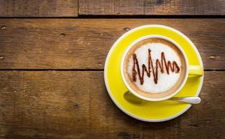 bovenaanzicht van latte koffie of cappuccino koffie in gele kop met latte art op houten tafel. foto