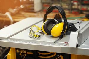 oorkappen en veiligheidsbril op elektrische zaagtafel in werkplaats. werkveiligheidsconcept. selectieve focus foto