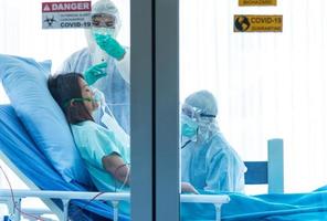 artsen in beschermend pak vaccineren en controleren de bloeddruk van de patiënt die is geïnfecteerd met corona visrus of covid-19 in de quarantainekamer in het ziekenhuis. foto