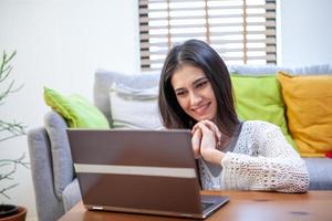 mooie jonge vrouw die op laptopcomputer werkt terwijl ze in de woonkamer zit foto