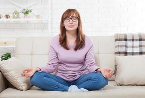 vrouw doet yoga thuis in de slaapkamer. vrouw van middelbare leeftijd die binnenshuis mediteert. yoga houding. levensstijl en menopauze concept foto