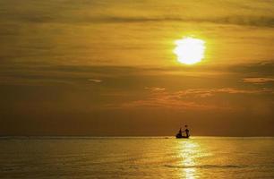 silhouet van een vissersboot van een klein dorp die 's ochtends naar zee gaat. de zee heeft golven en de zonnestralen in de ochtend. foto