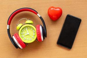 koptelefoon en wekker en smartphone en rood hart op houten bureau. muzikaal concept foto