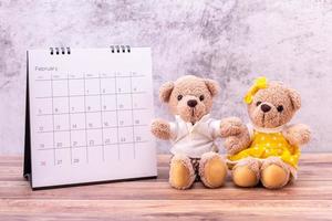 paar teddybeer met kalender op houten tafel. valentijnsdag viering foto