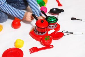 het kind speelt met gesneden plastic groenten en fruit met klittenband, kookt voedsel op een speelgoedfornuis in een kom. koken voor kinderen, een meisje leert koken. witte achtergrond, close-up, concept. foto