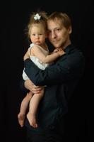 een vader houdt zijn eenjarige dochtertje in zijn armen. geschoten op een zwarte achtergrond. foto