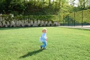 kleine blonde jongen zit op het groene gras. foto