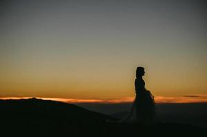 vrouw in trouwjurk rent over het veld naar de bergen foto