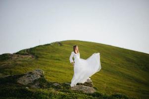 vrouw in trouwjurk rent over het veld naar de bergen foto