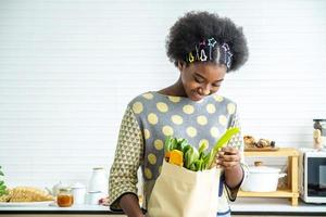 jonge gelukkige vrouw afro-amerikaanse afro-haar is net terug van de markt. en haalde de tomaat, citroen uit de papieren zak om te koken, gezondheidsconcept foto