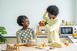 twee schattige schattige broers en zussen Afro-Amerikaanse kinderen die ontbijten met melk in de keuken, portret van gelukkige broer die melk drinkt met biceps om te vertellen met zijn zus, eten en drinken gezondheidszorg foto