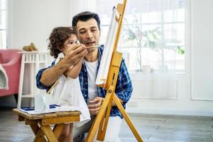 gelukkige familie van vader en kind tekenen foto, met behulp van verschillende verven en penselen. knappe vader en mooi dochtertje tegen oliefoto glimlachen, plezier maken. les van kunst foto