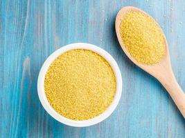 witte kom en houten lepel met rauwe couscous op blauwe houten ondergrond, bovenaanzicht. traditioneel Marokkaans eten foto